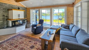 A cozy living room with a fireplace, a sofa, a table, and large windows offering a view of a lake.
