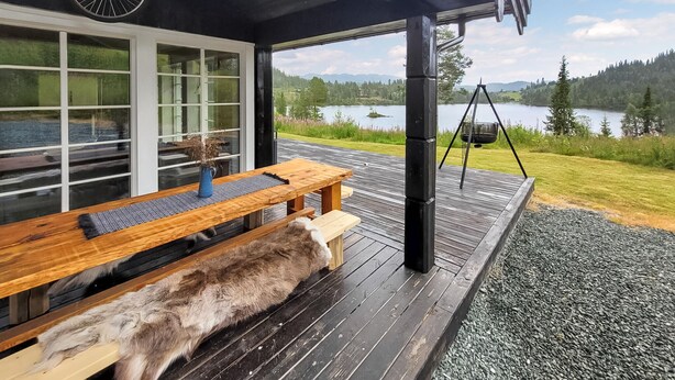 A wooden deck with a bench and a hanging swing chair, overlooking a lake and forested hills.