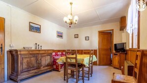 A dining area with a wooden table, chairs, a chandelier, and a television. - LE COLIBRI - BEAUFORT ARECHES (BEAUFORT ARECHES)