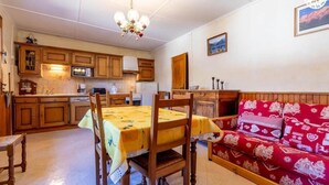 A dining area with a table and chairs, a sofa, wooden cabinets, a microwave, and a chandelier. - LE COLIBRI - BEAUFORT ARECHES (BEAUFORT ARECHES)