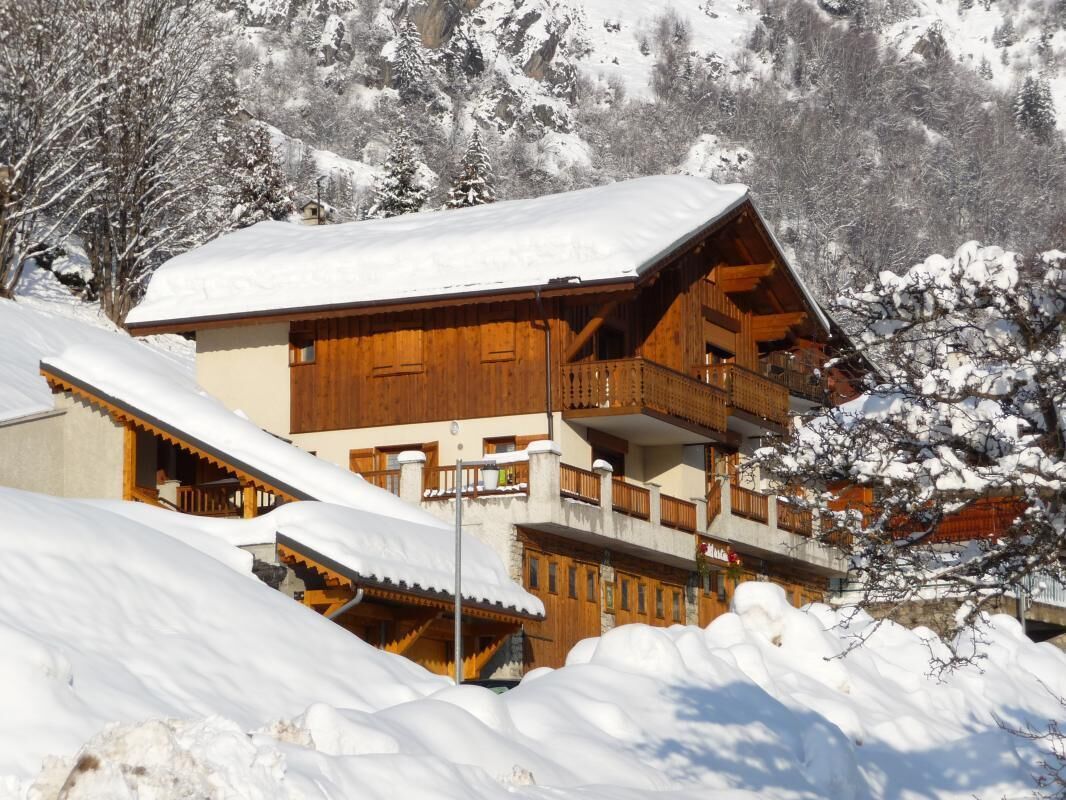 A wooden chalet with a balcony, surrounded by snow-covered mountains.