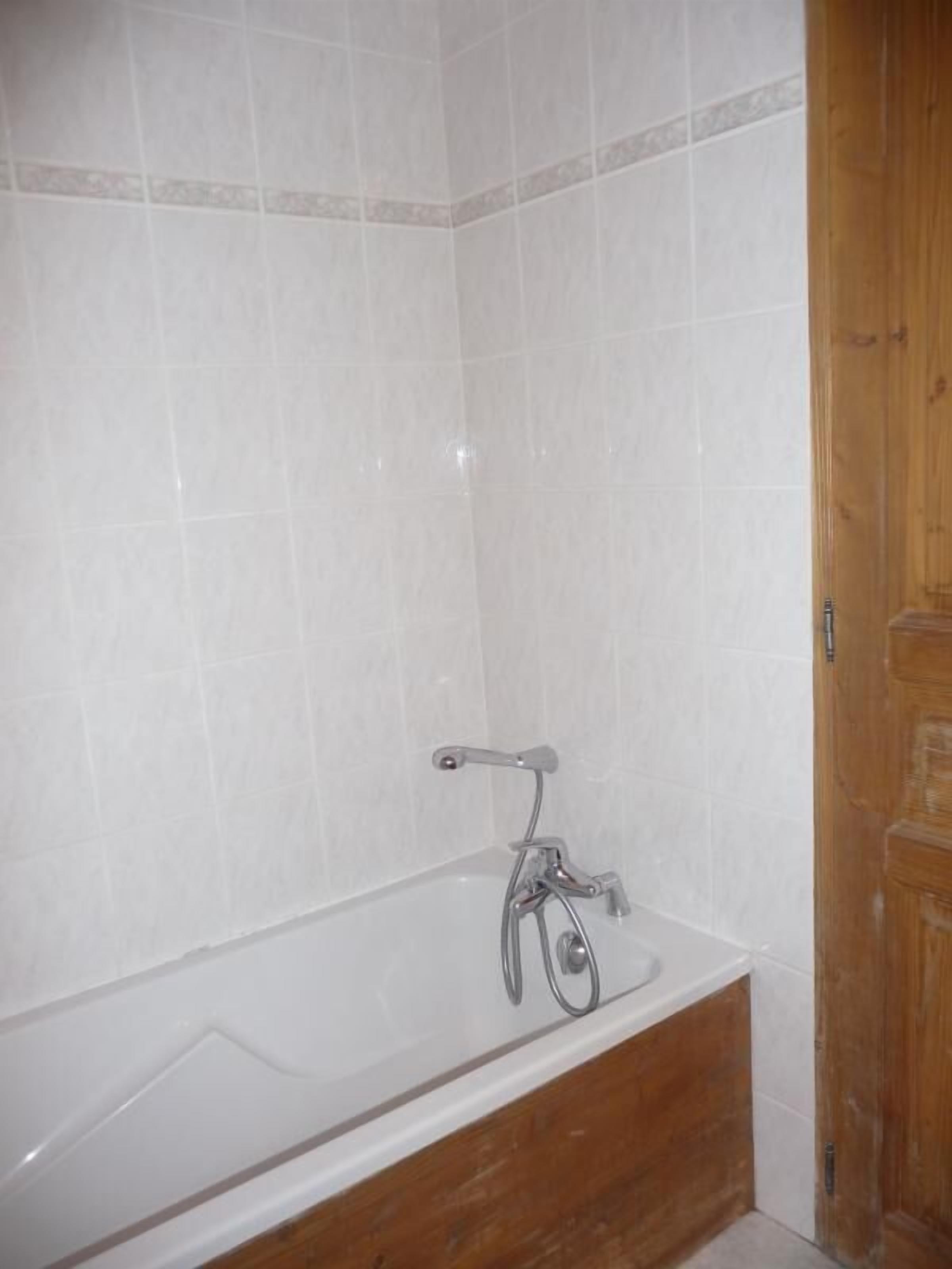 A bathroom with a white bathtub, wooden door, and tiled walls.