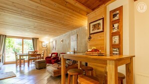 Ein gemütliches Zimmer mit Holzboden, einem Esstisch mit Hockern, einem roten Sofa und einem großen Fenster.