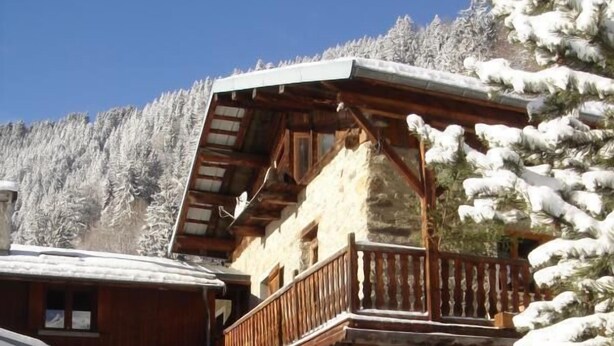 Eine Chalet mit Holzbalkon, Steinwänden und einem schneebedeckten Berg im Hintergrund.