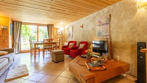 Ein gemütliches Wohnzimmer mit Holzbalkendecke, einem roten Sofa, einem Fernseher und einem Essbereich mit Holzmöbeln.