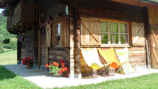 Un chalet rustique en bois doté d’un balcon, de grandes fenêtres et d’un espace salon extérieur.