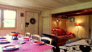 Interno di una baita in legno con zona pranzo, angolo relax e camino.