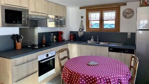 Une cuisine compacte avec des meubles en bois, un four à micro-ondes, une cuisinière et un évier. On y trouve une fenêtre avec des rideaux, une horloge et un petit réfrigérateur.