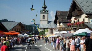 Un marché animé en plein air, avec des bâtiments en bois et une église en arrière-plan.