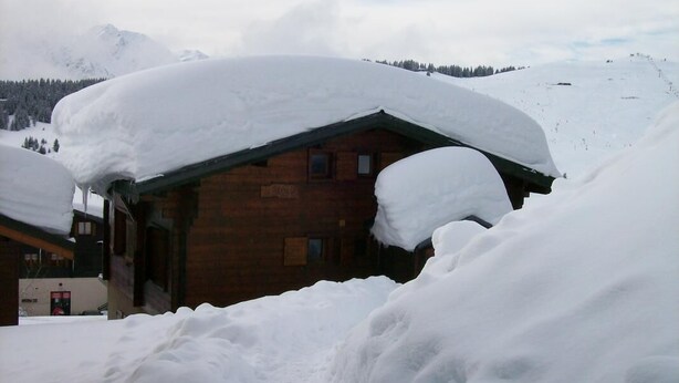Una cabana de fusta amb teulades cobertes de neu i un paisatge de muntanyes al fons.