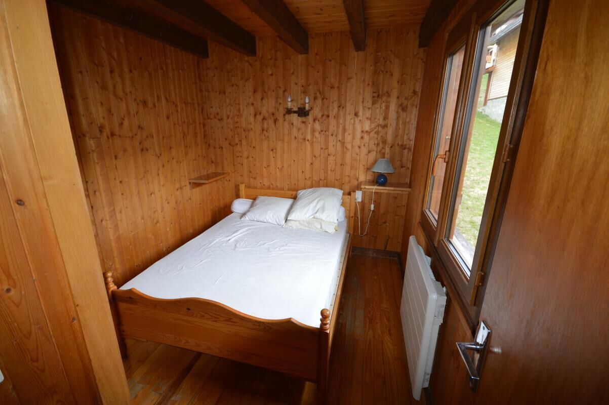 A wooden room with a bed, a nightstand, a lamp, and a window with a view of the outside.