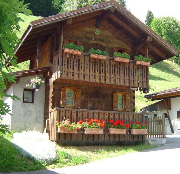 A wooden chalet with a balcony, flower boxes, and a sign reading 'LE NAIN'.