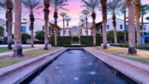 A courtyard with a central water feature, palm trees, and buildings with balconies. - Desert Crown Jewel Retreat in La Quinta #A (La Quinta)