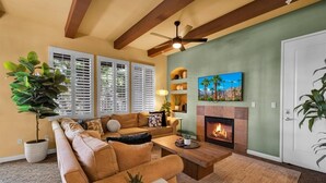 A living room with a sofa, coffee table, fireplace, TV, and potted plants. - Desert Crown Jewel Retreat in La Quinta #A (La Quinta)