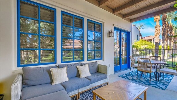 A covered patio area with a grey sofa, a wooden table, and a blue door. - Desert Crown Jewel Retreat in La Quinta #A (La Quinta)