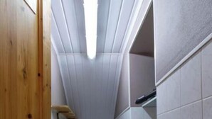 A narrow hallway with a wooden door on the left, a white tiled floor, a white tiled wall, and a white ceiling with a light fixture. - Le Myosotis - VAL CENIS (VAL CENIS)