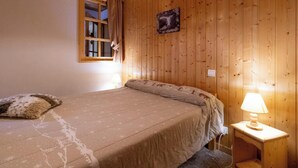 A bedroom with a bed, a nightstand with a lamp, wooden walls, a window with curtains, and a wall-mounted picture. - Le Myosotis - VAL CENIS (VAL CENIS)