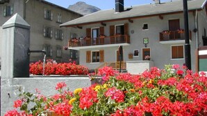 A building with a balcony, a stone pillar, and a flower bed with red flowers. - Le Myosotis - VAL CENIS (VAL CENIS)