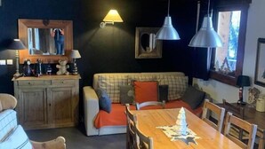 Ein gemütliches Wohnzimmer mit Holzboden, einer Couch, einem Esstisch und Pendelleuchten.