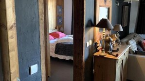 Ein Zimmer mit Holzbalkendecke, einem Bett mit rosa Bettwäsche, einem Schminktisch mit Lampen und einem Spiegel an der Wand.