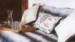 Ein gemütliches Blockhaus-Interieur mit einer Holzwand, einem Hirschbild in einem Rahmen, einer Couch mit gemusterten Kissen und einer Ablage mit Gläsern und einer Kerze.