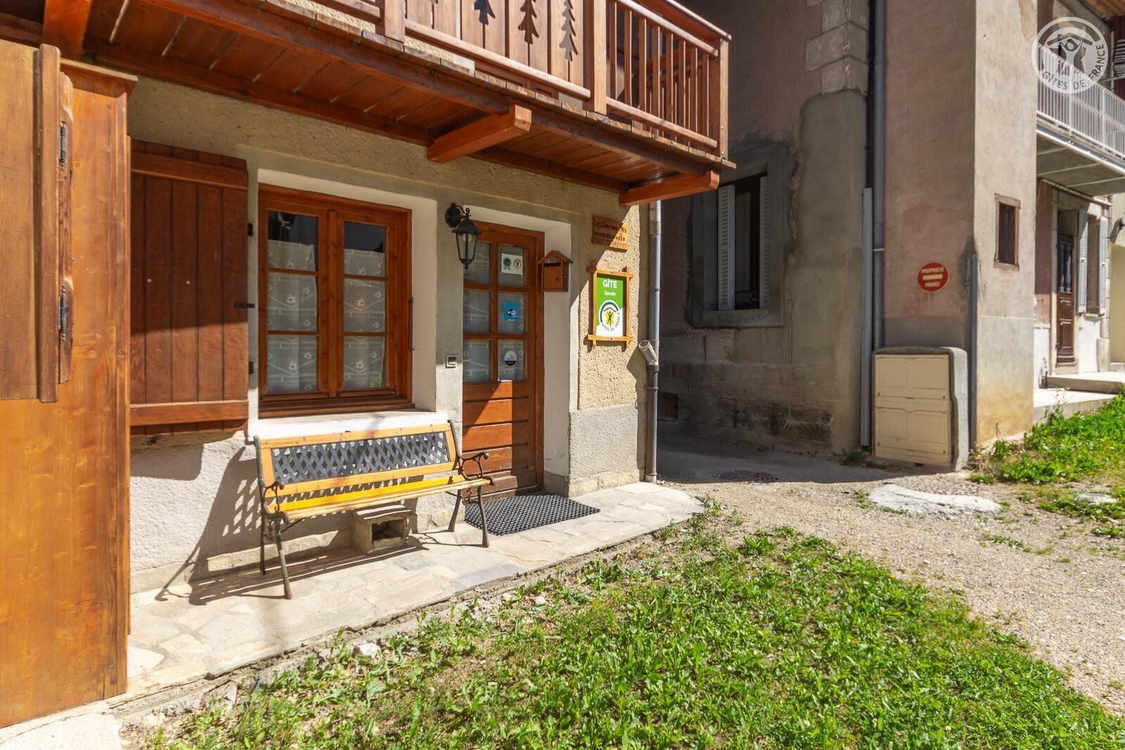 A building with a wooden balcony, a bench outside, and a sign indicating it's a gîte.
