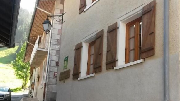 Edifici de dues plantes amb persianes de fusta, una entrada ben visible i un carrer al davant.
