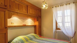 A bedroom with a wooden headboard, a bed with a colorful striped bedspread, a hanging light fixture, and a window with sheer curtains. - LES CAMPANETTES 1st floor (PRALOGNAN LA VANOISE)