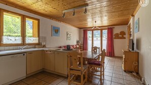 Una cocina con armarios de madera, una mesa de comedor con sillas, un lavamanos y un ventanal con cortinas.