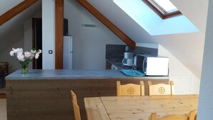 A kitchen with a wooden counter, a microwave, and a coffee maker. There is a skylight above the counter, and a dining table with chairs in the foreground. - ECOLE A GITER - LA GELINOTTE (SAINT FRANCOIS DE SALES)