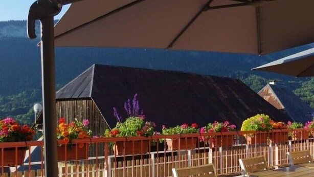 An outdoor patio with a wooden table and chairs, surrounded by flower planters and a large umbrella. - ECOLE A GITER - LA GELINOTTE (SAINT FRANCOIS DE SALES)