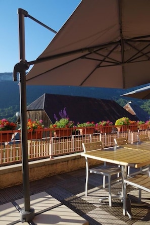 An outdoor patio with a wooden table and chairs, surrounded by flower planters and a large umbrella.