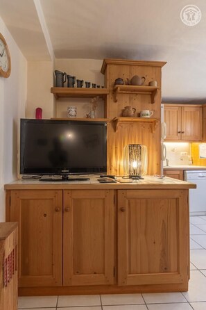 Un îlot de cuisine en bois, doté d’un téléviseur à écran plat, d’une lampe et de divers ustensiles de cuisine rangés sur des étagères.