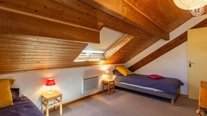 A bedroom with a sloped ceiling, a skylight, a heater, a bed, a bedside table with a lamp, and a door. - LE TALAPET - CONFETTI (ALBIEZ MONTROND)