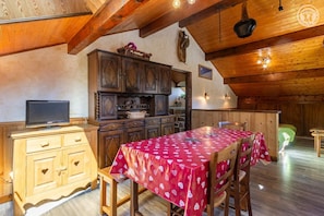 A cozy dining area with a red tablecloth, wooden cabinets, and a television on a wooden cabinet. - LES JONQUILLES - VALLOIRE (VALLOIRE)