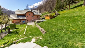 Ein Haus mit schrägem Dach, einer Steintreppe und einem Garten mit einer Holterrasse.