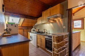 A compact kitchen with wooden cabinets, a built-in washing machine, and a stone accent wall. - LES JONQUILLES - VALLOIRE (VALLOIRE)