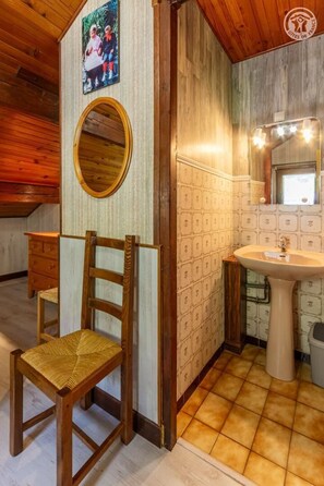 Une salle de bain avec une chaise en bois, un miroir, un lavabo et des carreaux à motifs.