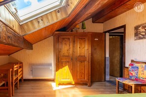 A room with a sloped ceiling, wooden furniture, a door, and a painting on the wall.