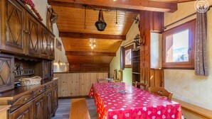 Ein Holzinnenraum mit einem langen Esstisch, der mit einer roten Tischdecke bedeckt ist, Holzschränken und einer hängenden Leuchte.