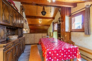 A wooden interior with a long dining table covered in a red tablecloth, wooden cabinets, and a hanging light fixture. - LES JONQUILLES - VALLOIRE (VALLOIRE)