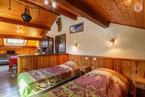 A cozy room with wooden walls and ceiling, two beds with floral bedding, a small table, and a wooden cabinet. - LES JONQUILLES - VALLOIRE (VALLOIRE)
