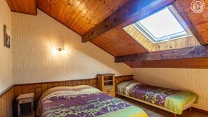 Ein Schlafzimmer mit zwei Betten, einem Oberlicht, Holzbalken und einem Nachttisch.