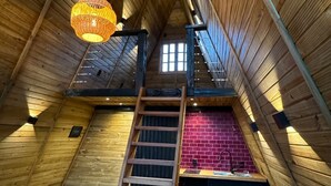 Une pièce mansardée aux murs en bois, avec une échelle en bois, un mur en briques et un luminaire suspendu.