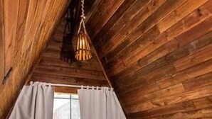 Une pièce chaleureuse, aménagée dans un chalet en bois, avec un lit, une télévision et une fenêtre avec des rideaux.