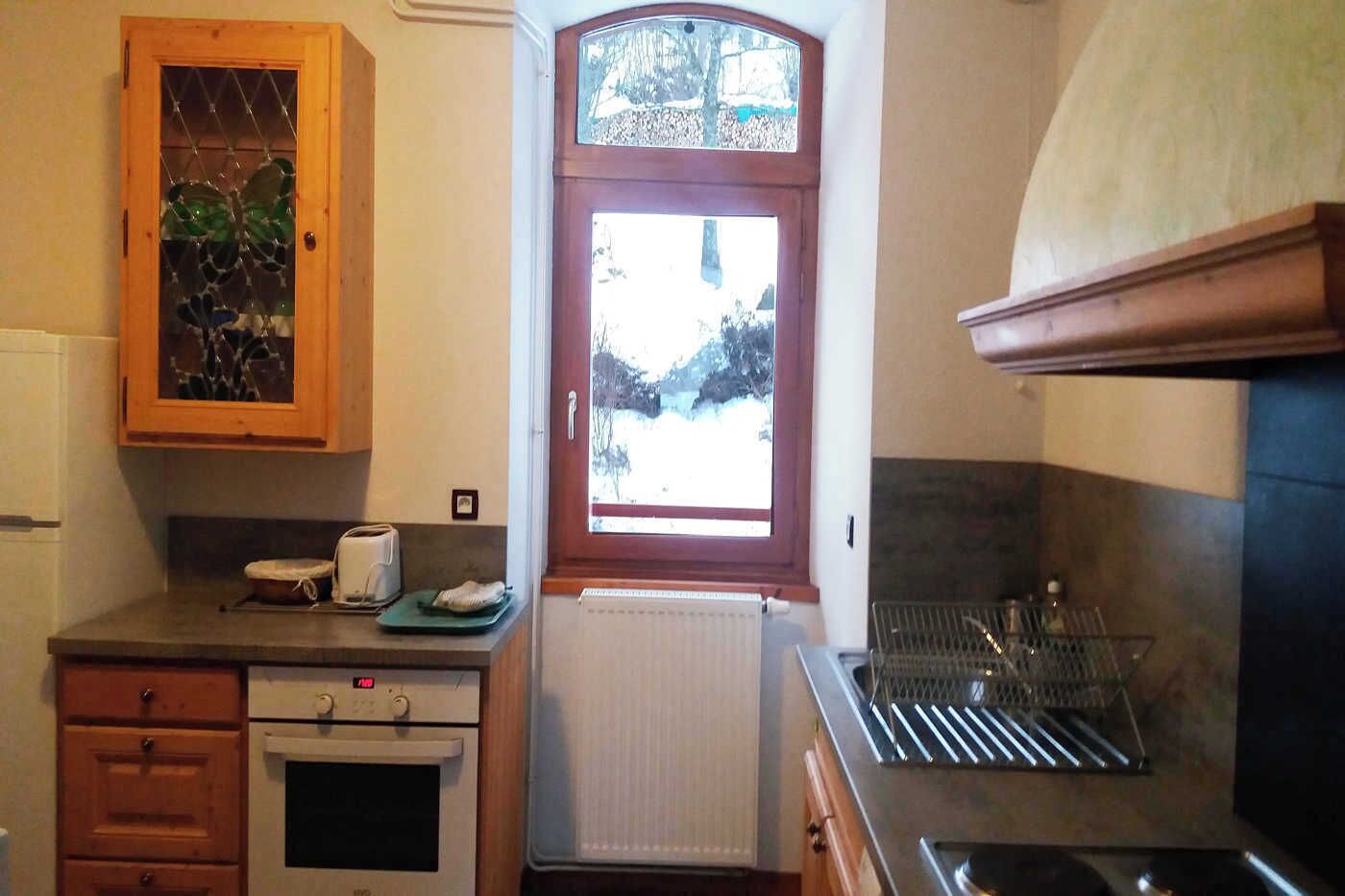 A compact kitchen with a wooden cabinet, a window with a view, a built-in oven, and a dish rack.