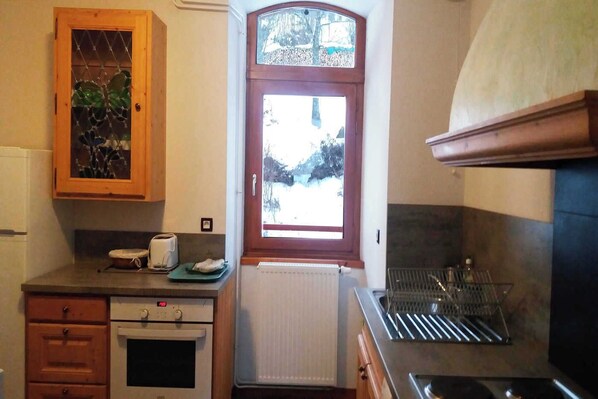 A compact kitchen with a wooden cabinet, a window with a view, a built-in oven, and a dish rack.