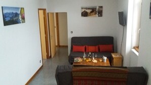 Une pièce comprenant un canapé, une table basse avec des boissons, un téléviseur et des œuvres d’art accrochées aux murs.