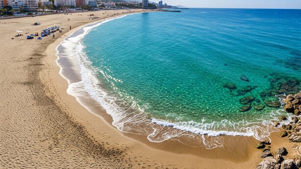 A beach with clear turquoise waters, a sandy shore, and a cityscape in the background.