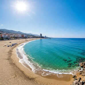 Ein Strand mit klarem türkisblauem Wasser, einem sandigen Ufer und einer Stadtkulisse im Hintergrund.